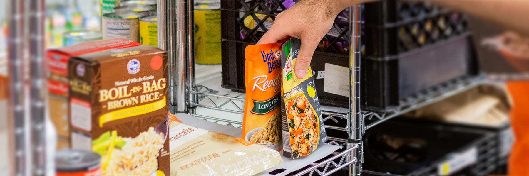 a hand placing packets of rice on a metal storage shelf