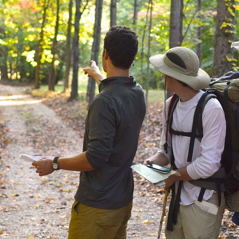 two hikers look at a trail map, one points into the distance