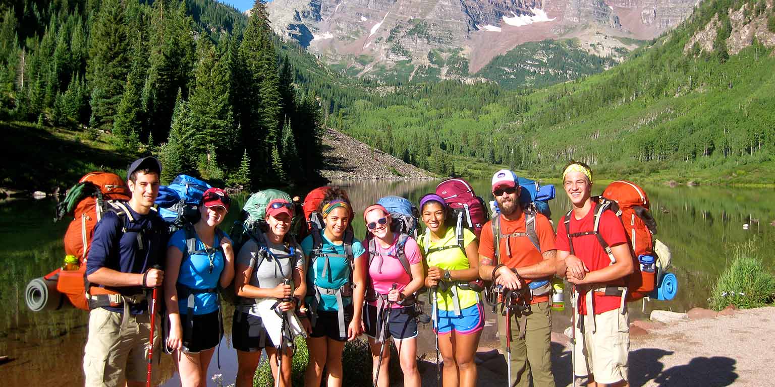 nine backpackers pose in front of a mountain vista
