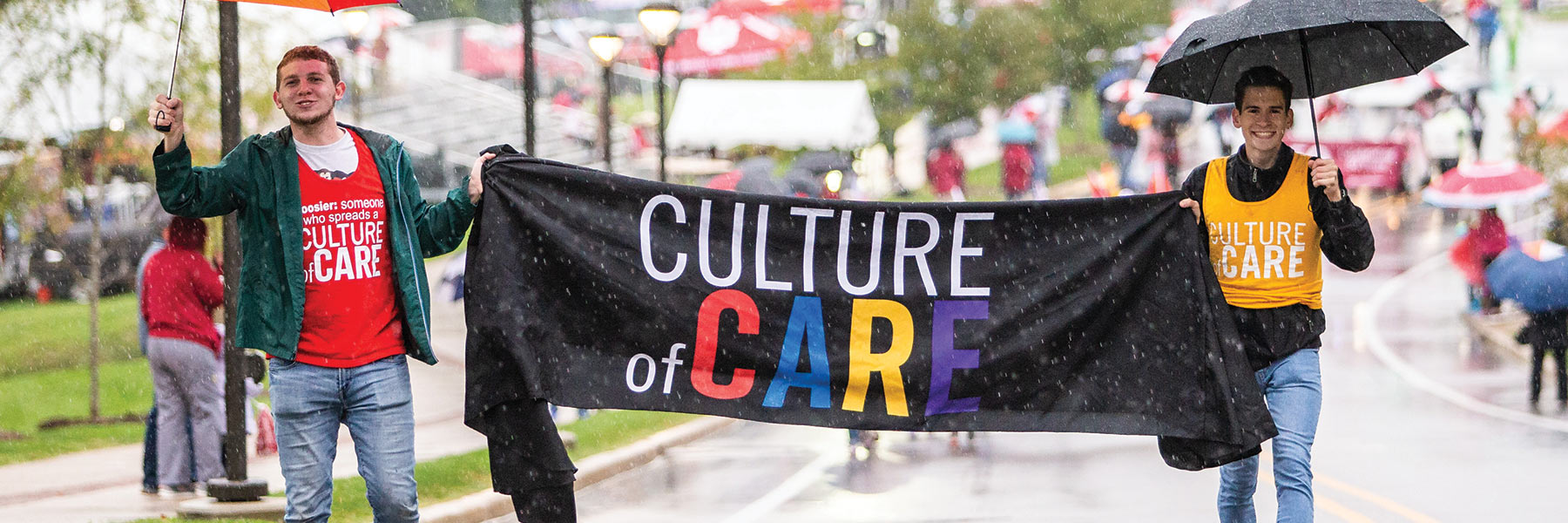 students walking  in a rainy parade, holding a banner that says culture of care
